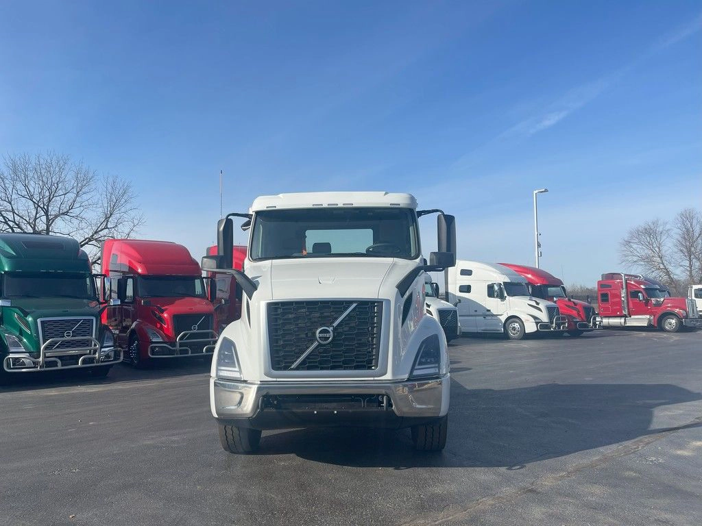 Front view of a white Volvo VNR day cab with black grille, parked in a truck dealership lot.