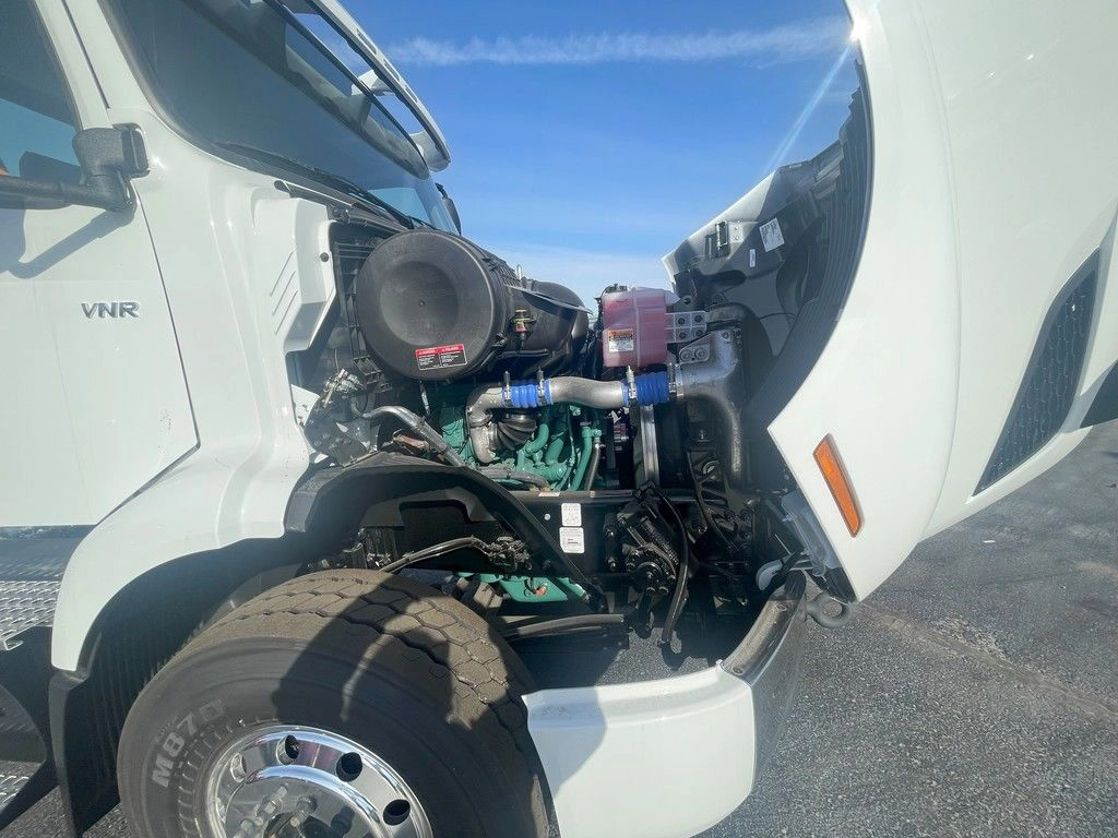 Close-up of the white Volvo VNR engine area with the hood open, showing hoses and front wheel.