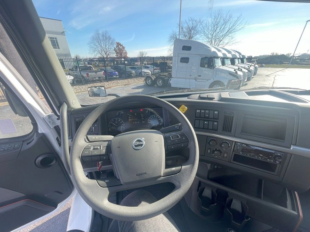 Volvo VNR driver cockpit with steering wheel, dashboard controls and windshield view of the lot.