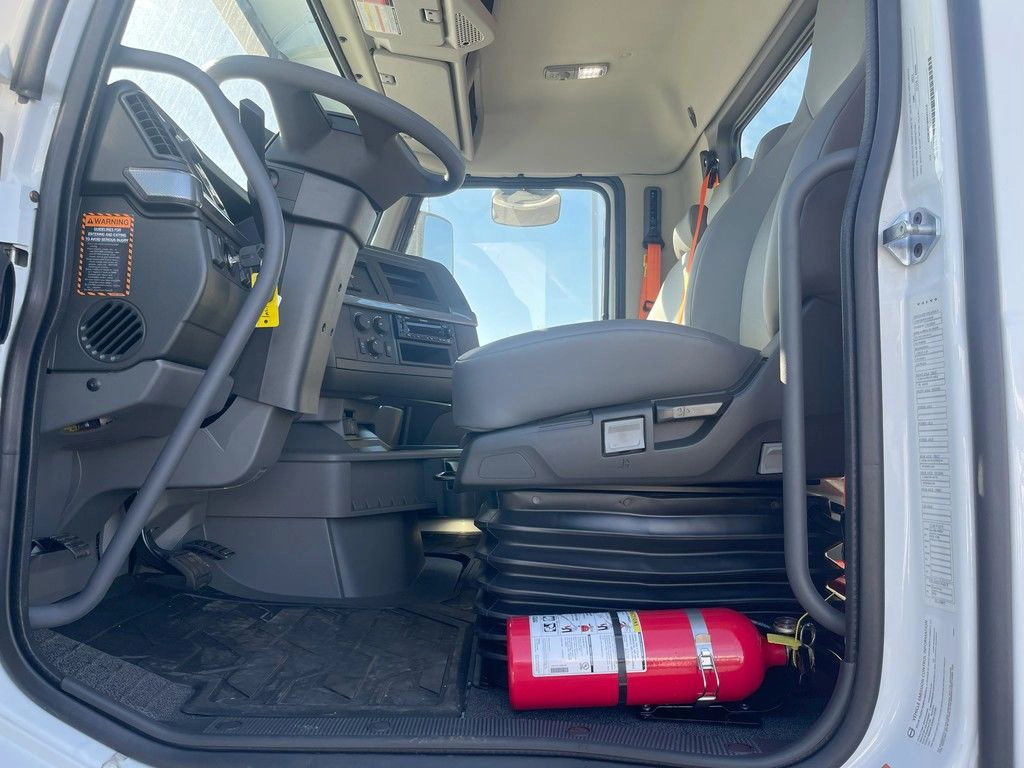 Open Volvo VNR cab entry showing the driver seat, gray floor and red fire extinguisher.