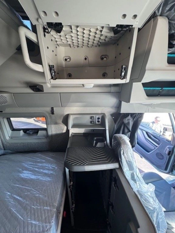 Interior of a Volvo VNL truck sleeper cab showing a lower bed, an upper bunk in the raised position, a small ladder, and storage compartments.