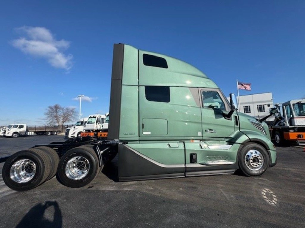 Side view of a green Volvo VNL sleeper cab with aerodynamic fairings and tandem rear axles.