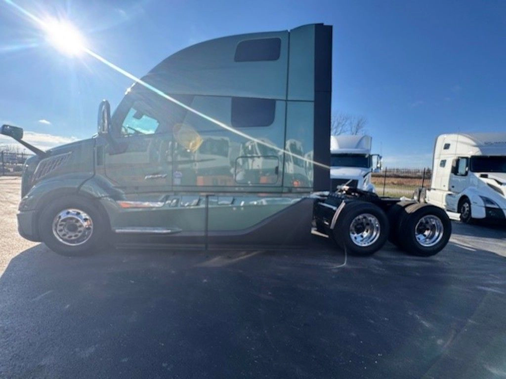 Driver-side view of a green Volvo VNL sleeper cab parked in a lot, with sun glare across the cab.