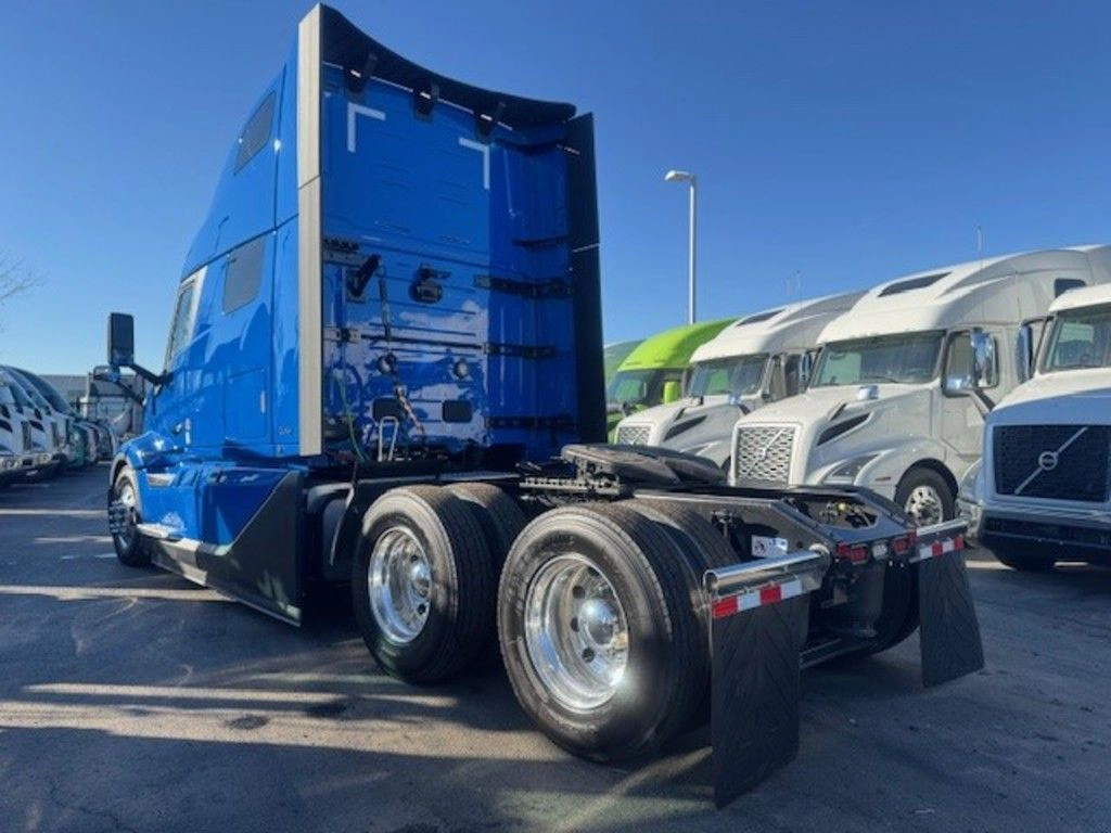 A bright blue semi-truck cab is parked in a lot, surrounded by several other trucks in different colors. The sky is clear and the mood is calm.