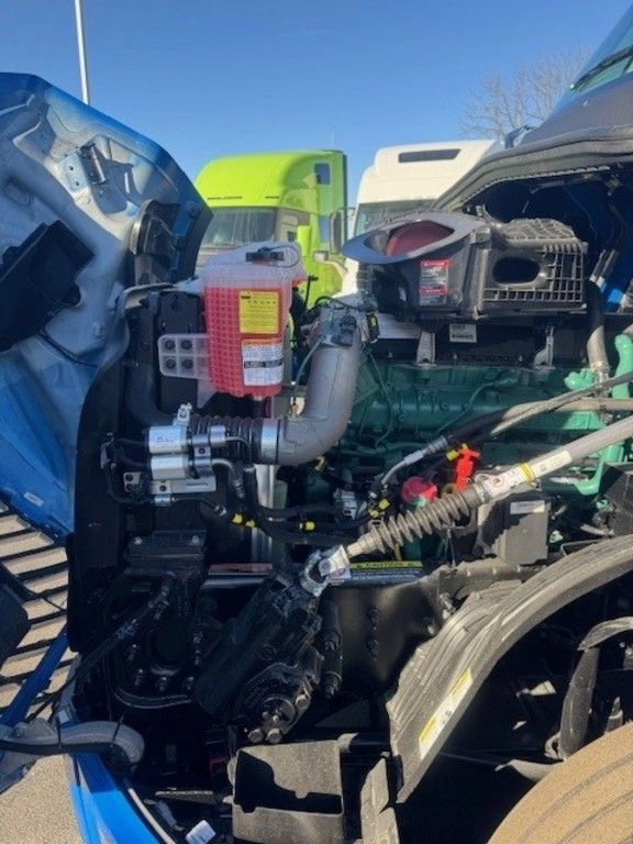 Volvo VNL engine bay with hood open, showing coolant reservoir, hoses and engine components.