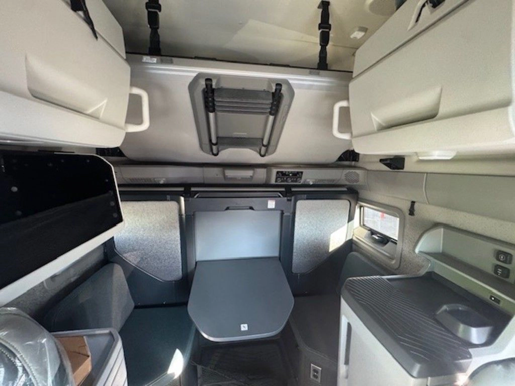 Volvo VNL sleeper area with upper cabinets, table, wrapped bunk and built-in storage.