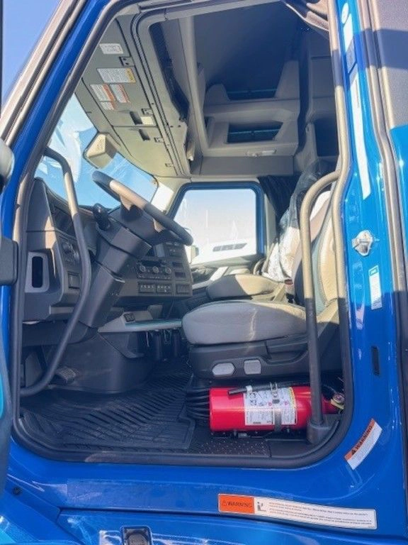 Driver-side view into a blue Volvo truck cab with seat, steering wheel and floor area.