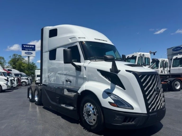 Front three-quarter view of a white Volvo VNL sleeper cab with black grille and tandem rear axles.