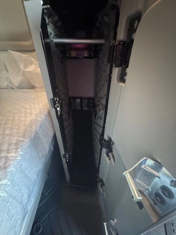 Tall interior storage compartment in the Volvo VNL660 sleeper next to the bunk and cab walkway.