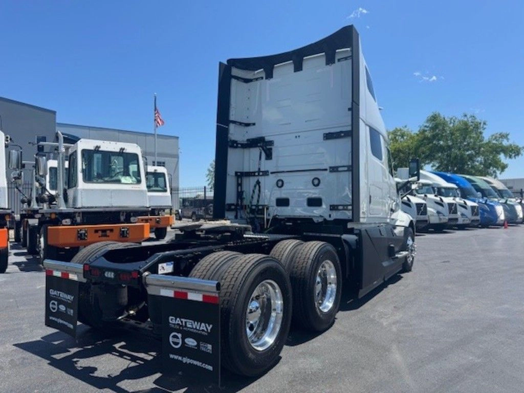 Rear three-quarter view of a white 2025 Volvo VNL660 sleeper tractor showing tandem axles and mud flaps.