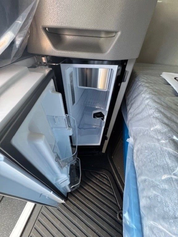 Open cabinet in Volvo VNL sleeper showing compact refrigerator and interior storage space.