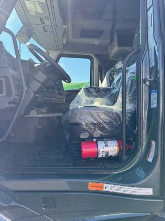 Open driver-side door showing Volvo VNL cab entry, wrapped seat, steering wheel and floor mat.