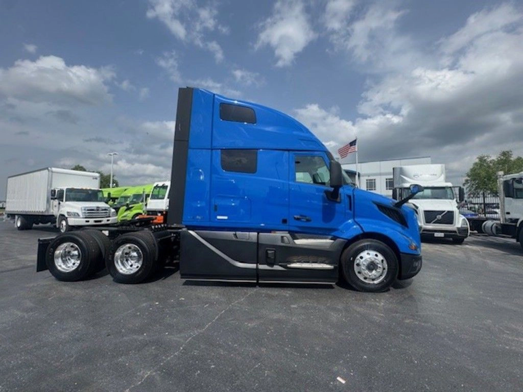Passenger-side profile of a blue Volvo VNL sleeper truck with gray lower fairings on the dealership lot.