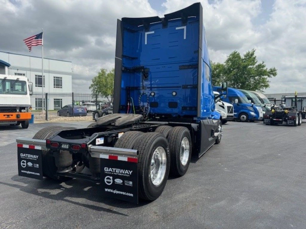 Rear passenger-side view of a blue Volvo VNL sleeper truck with polished wheels and fifth wheel.