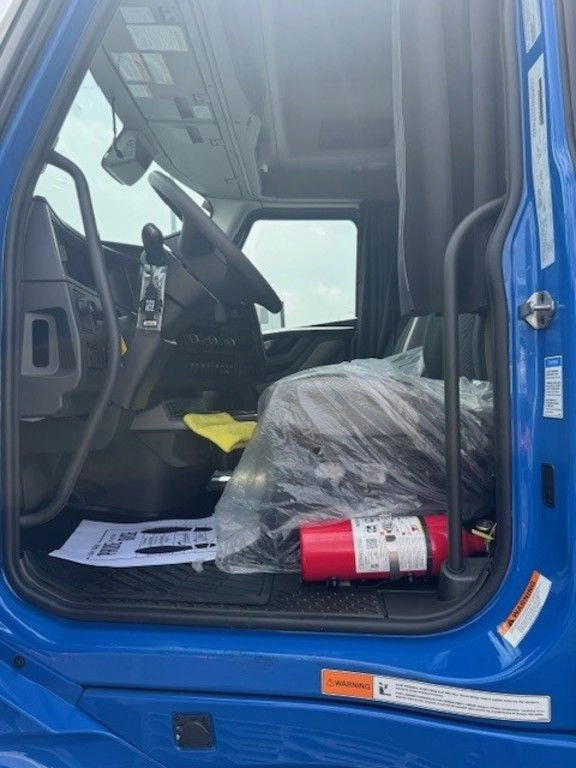 Open driver-side door showing the Volvo VNL cab entry, seat, floor mat and fire extinguisher.
