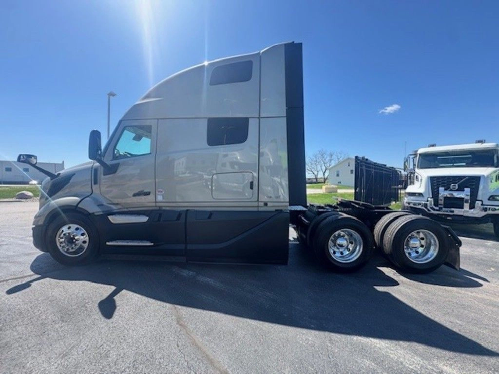 Side profile of a Volvo VNL sleeper tractor with gray cab, tandem axles and fifth wheel on the lot.