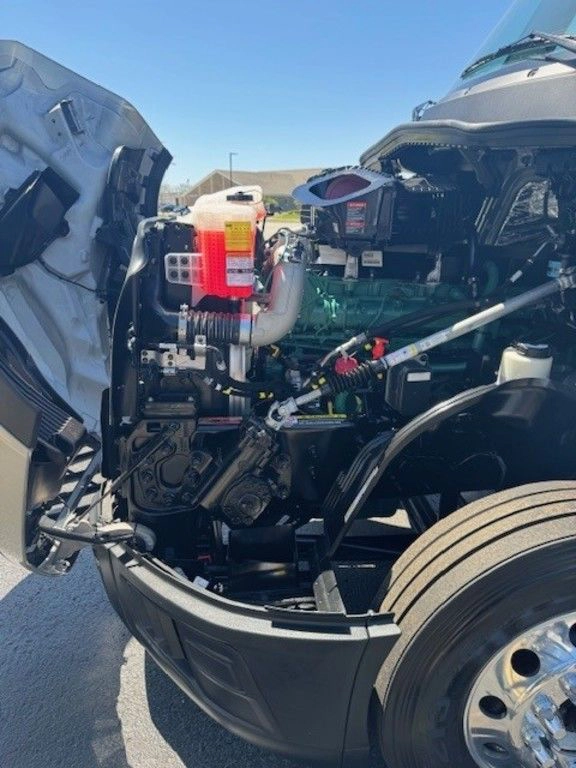 Open hood view of a Volvo VNL engine bay, showing powertrain components and service access on the dealership lot.