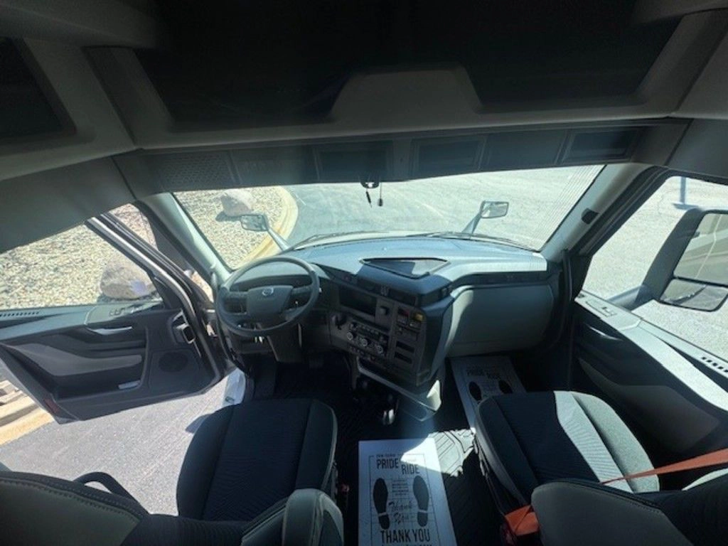 Wide interior view of the Volvo VNL cab showing the dashboard, windshield, seats and open driver door.