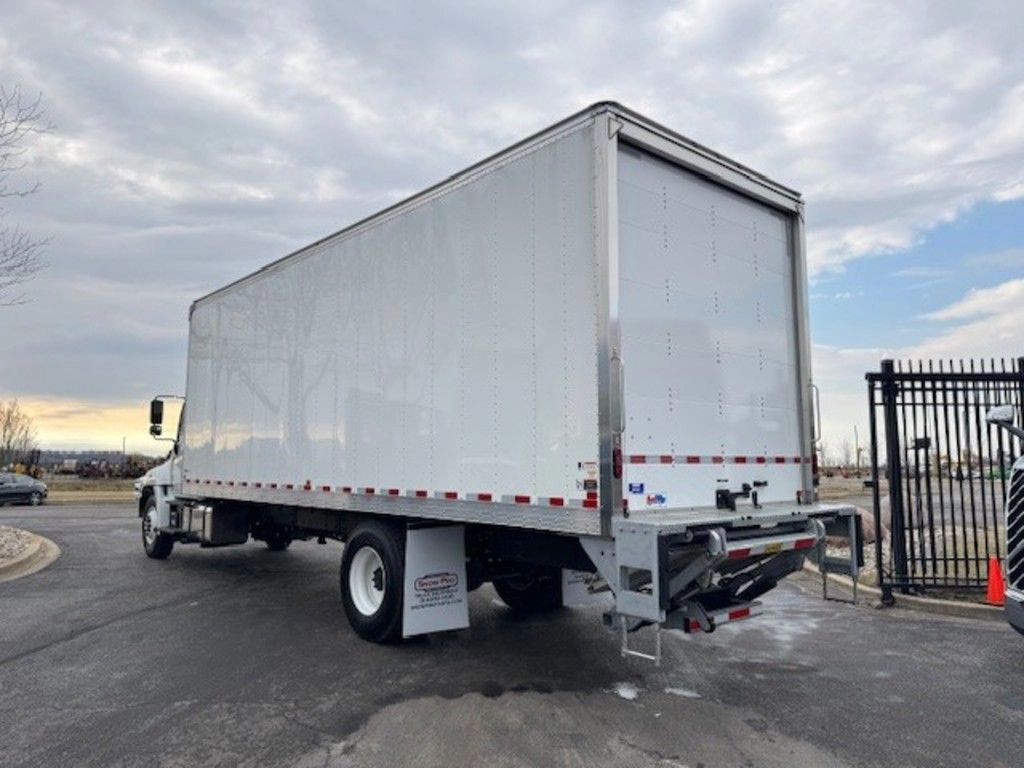 Rear driver-side view of the Hino L6 box truck with liftgate, rear bumper and white cargo body visible.