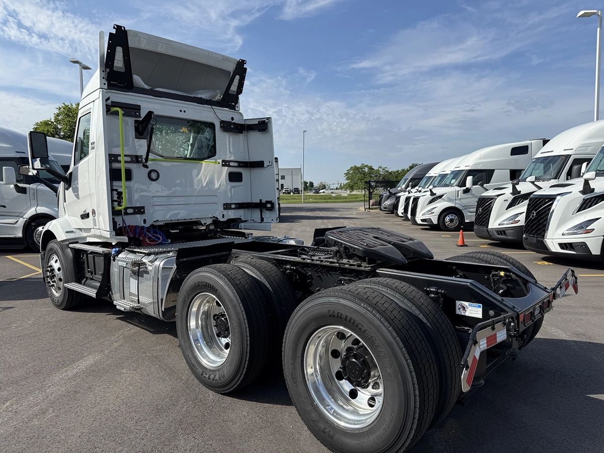Rear view of a 2027 Volvo VNR64T300 white day cab semi truck, showing the fifth wheel plate, dual rear axles, and tail lights in a dealership lot