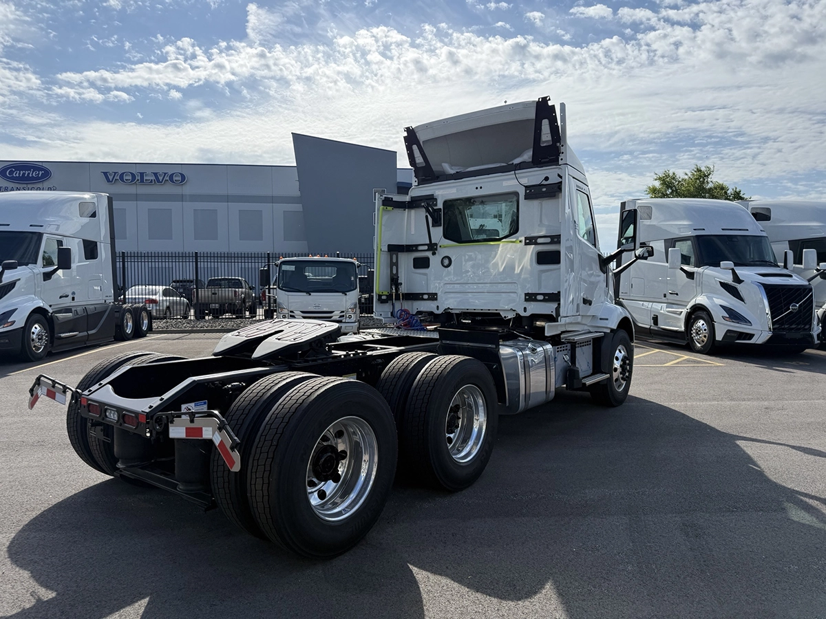 Rear view of a 2027 Volvo VNR64T300 white day cab semi truck, showing the fifth wheel plate, dual rear axles, and tail lights in a dealership lot