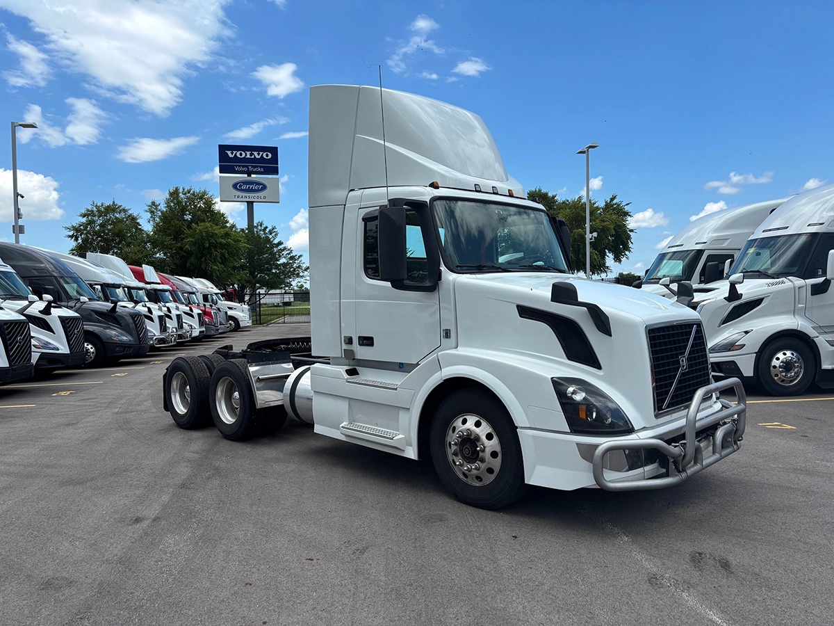 White 2017 Volvo VNR64T300 sleeper cab truck tractor, front driver-side view, parked at a dealership lot with other trucks in the background.