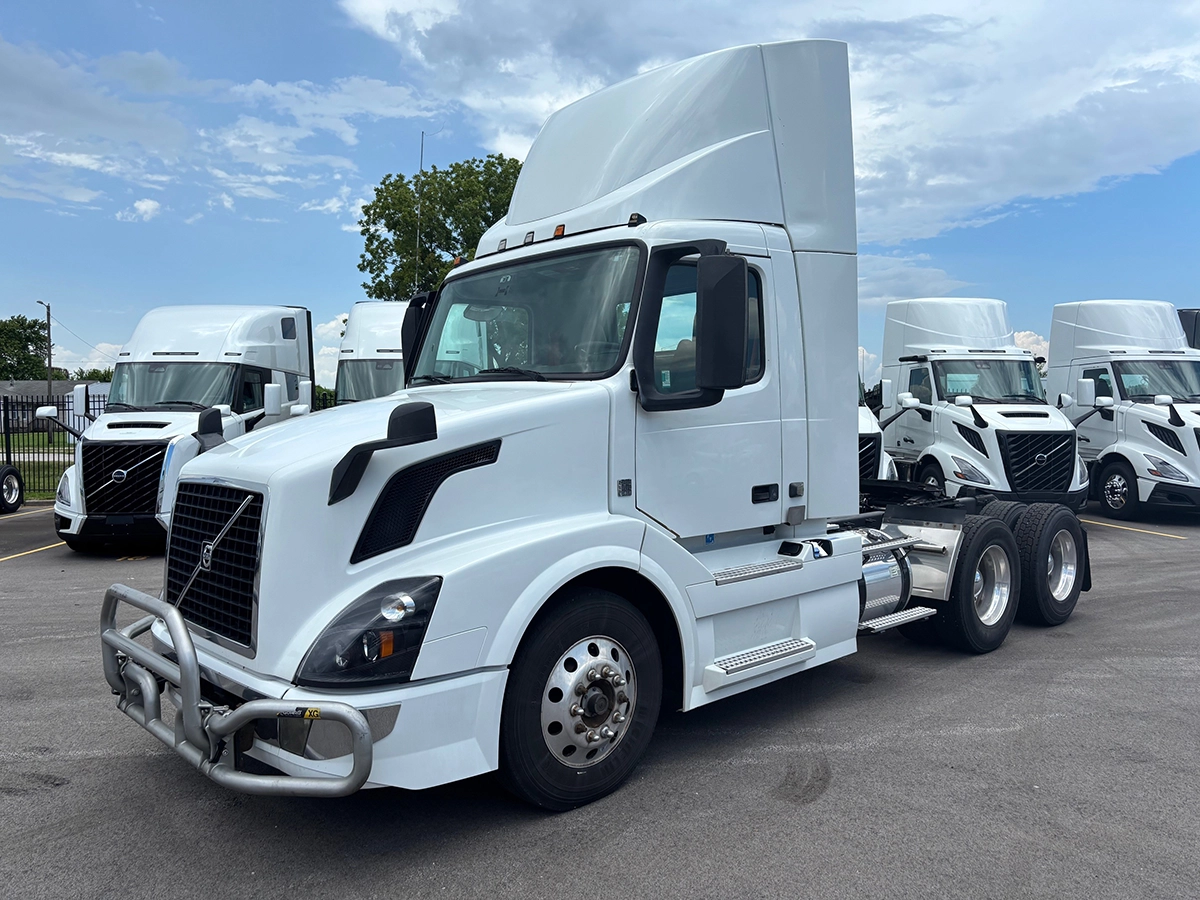 Front driver-side view of a white Volvo VNR sleeper cab truck tractor, parked among other white Volvo trucks.
