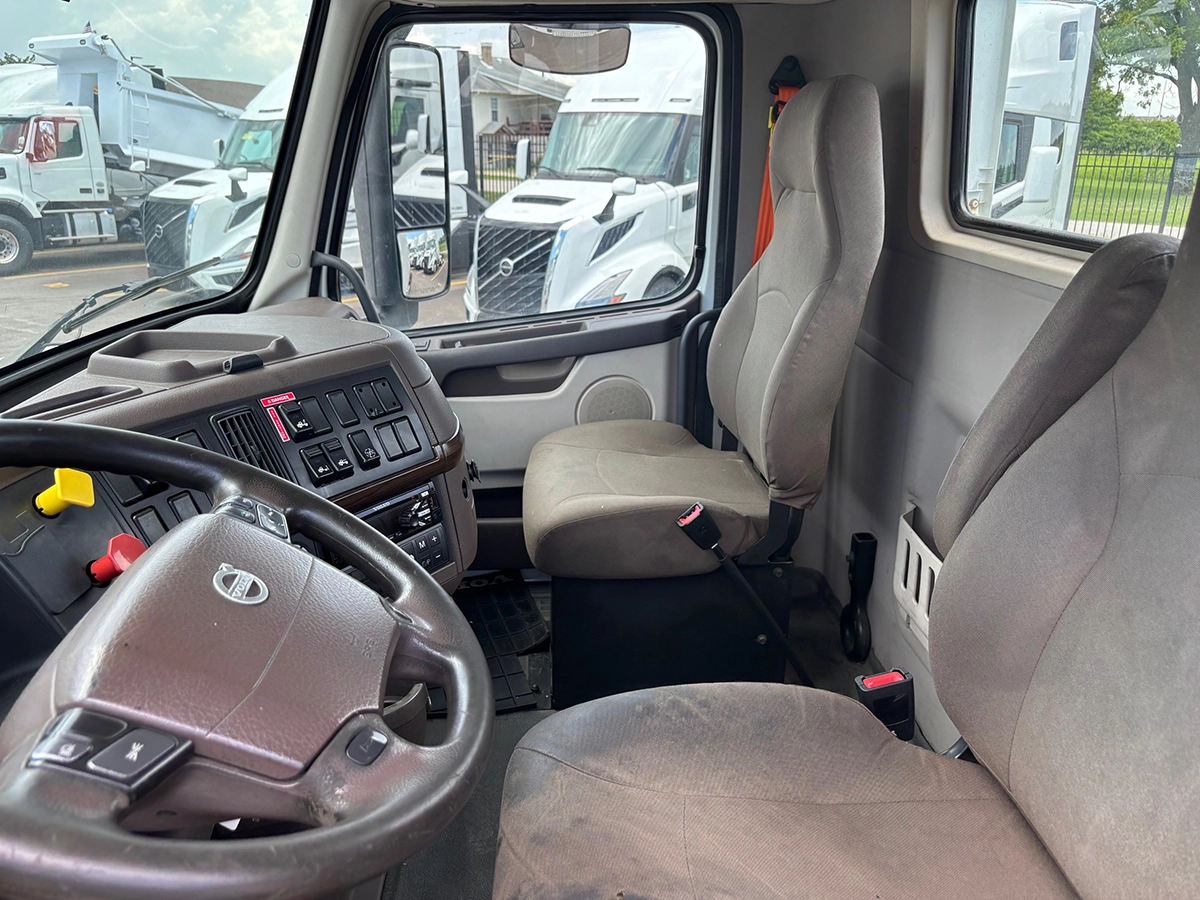 Interior view of the Volvo truck cab showing the steering wheel, dashboard controls, and two gray cloth seats.
