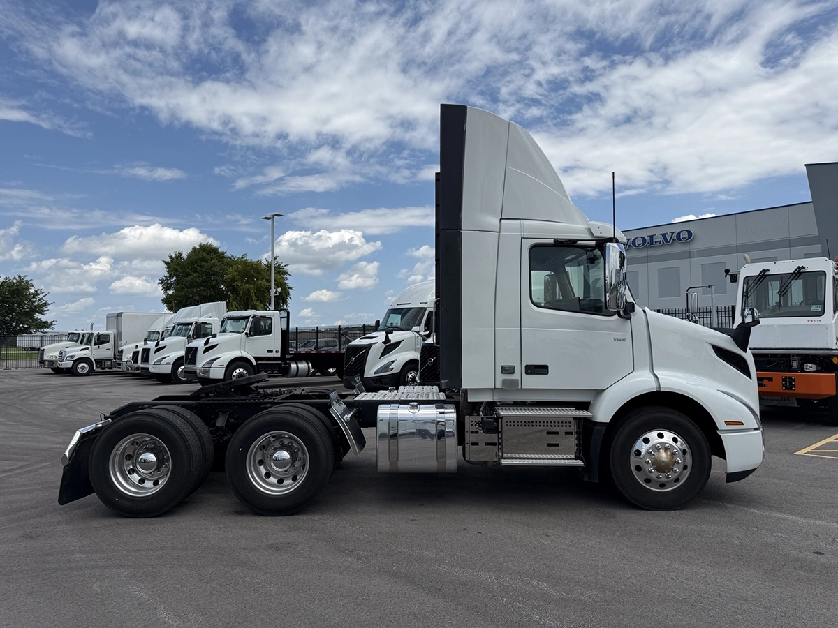 Driver's side profile view of the white Volvo VNR day cab truck tractor parked alongside several similar white Volvo trucks at the dealership.