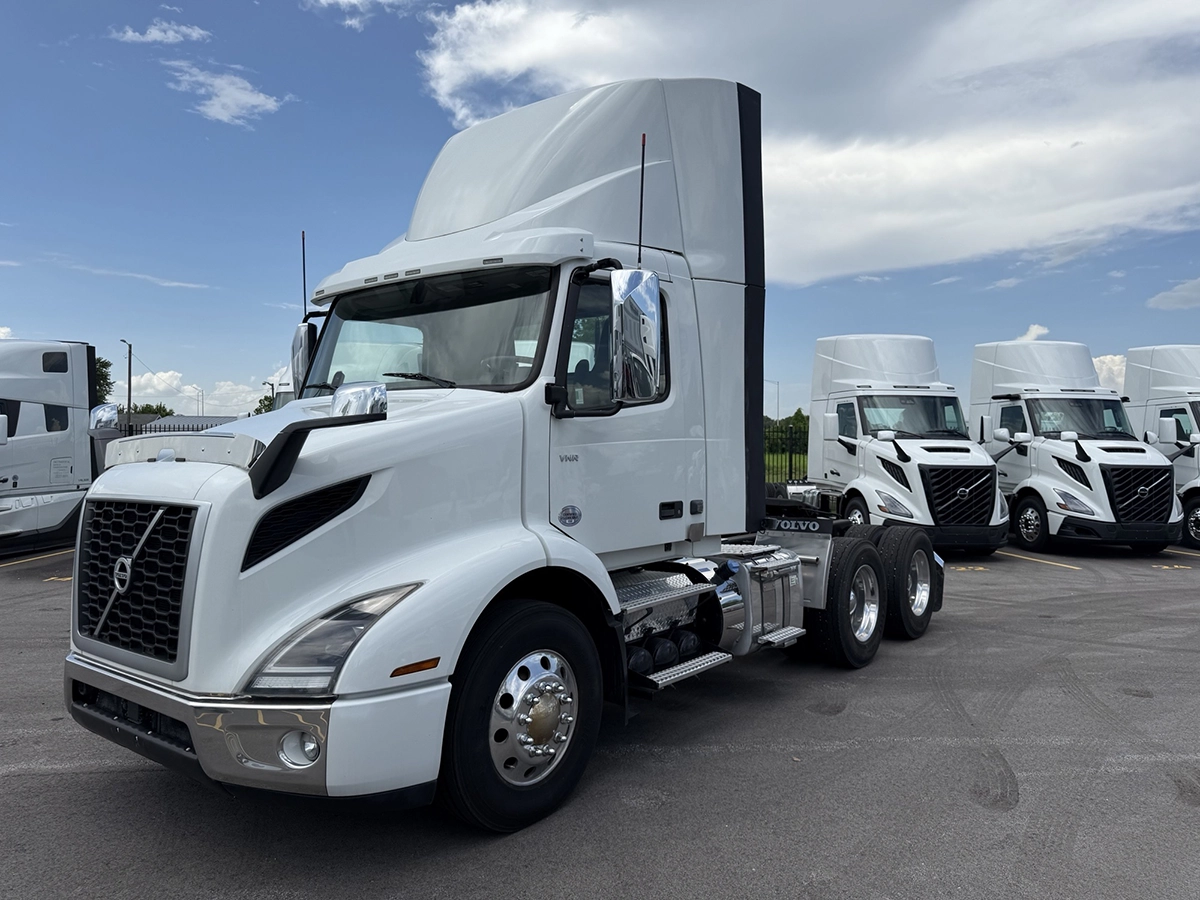 Front three-quarter view of the white Volvo VNR day cab truck tractor, showing the grille and cab, parked next to other Volvo trucks.