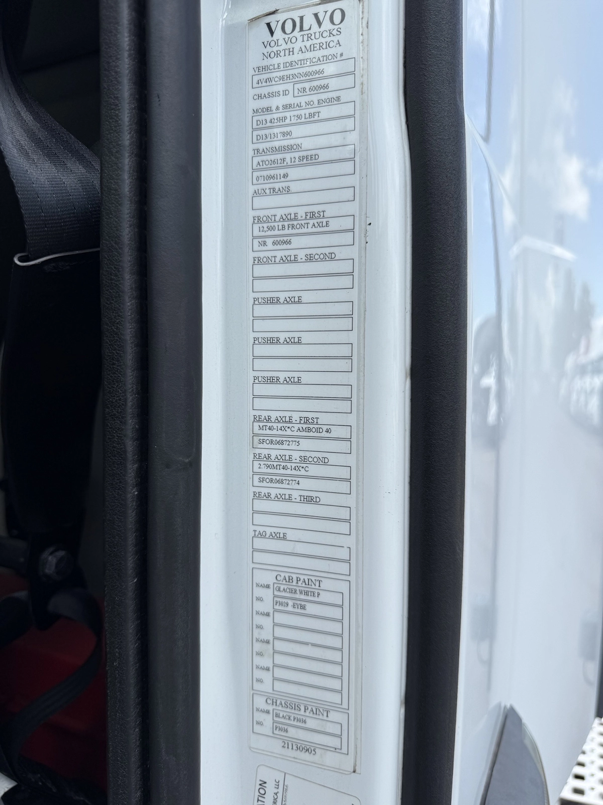 Close-up of the Volvo vehicle identification and specification data plate on the cab doorframe, listing VIN, chassis ID, engine, transmission, axle, and paint information.