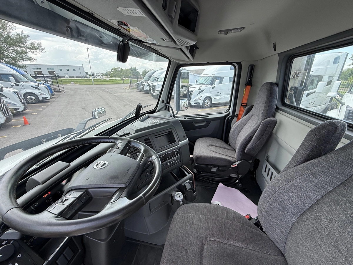Interior view of the Volvo truck cab showing the steering wheel, dashboard, and two gray cloth seats.