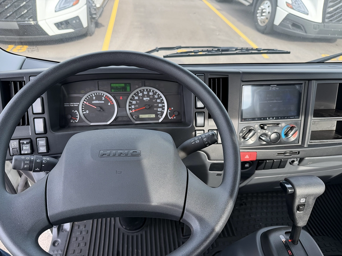 Interior cab view of a 2023 Hino S4 showing the steering wheel, gauge cluster, and dashboard infotainment screen.