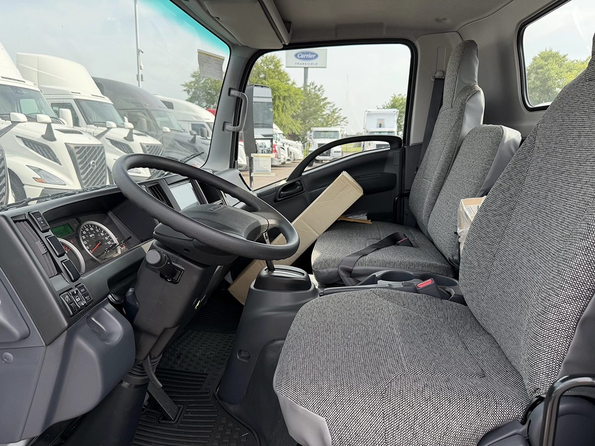 Interior cab view of a 2023 Hino S4 showing the steering wheel, dashboard, and gray cloth bench seating.