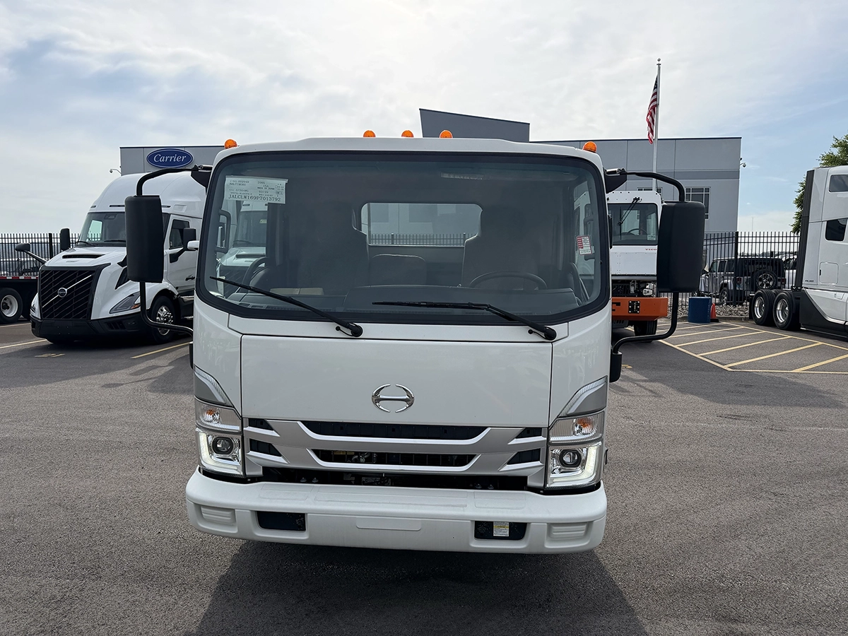 Front view of a white 2023 Hino S4 truck with a chrome grille and dual side mirrors, parked at a dealership lot.