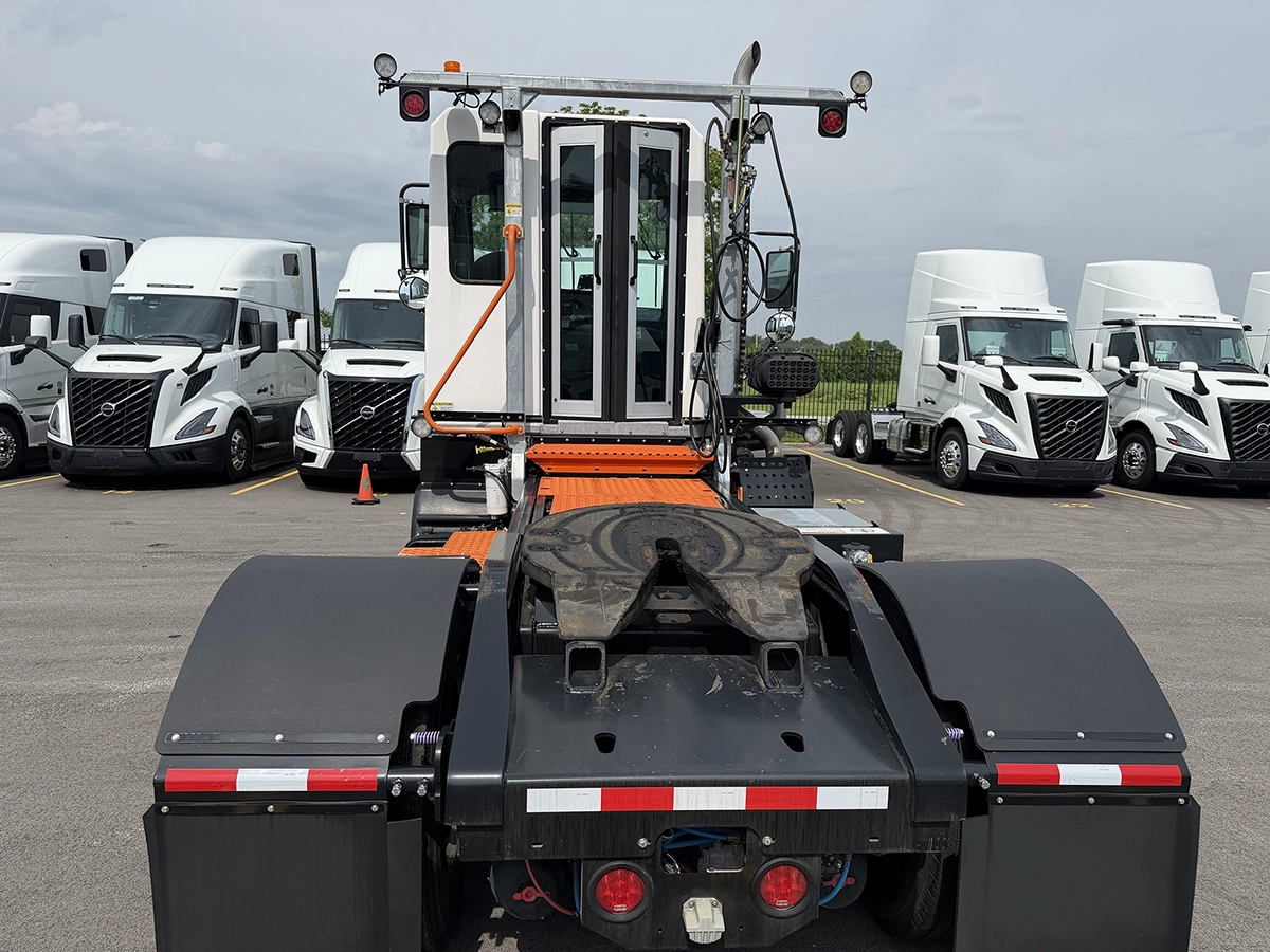 Rear view of a 2024 TICO Pro-Spotter yard truck showing the black fifth wheel, orange safety guides, and warning light bar, parked among rows of Volvo sleeper trucks.