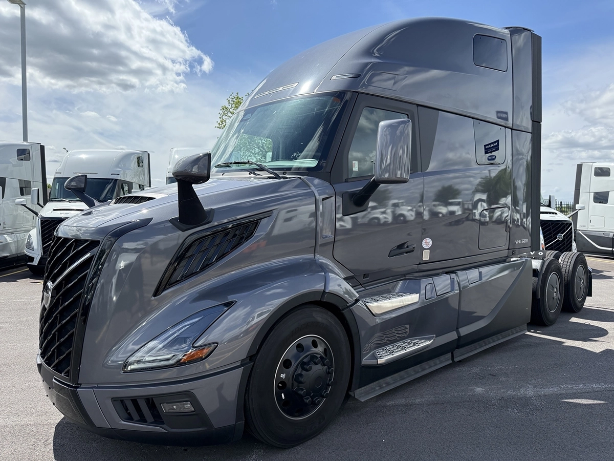 Front driver side view of a gray 2025 Volvo VNL64T860 sleeper semi truck with a black grille and aerodynamic high-roof sleeper cab.