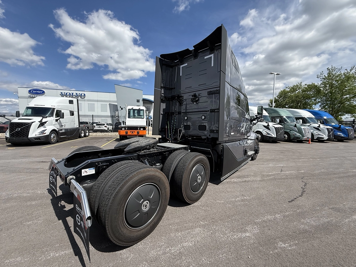 Rear passenger side view of a gray 2025 Volvo VNL64T860 showing the fifth wheel, tandem drive axles, and rear of the sleeper cab.
