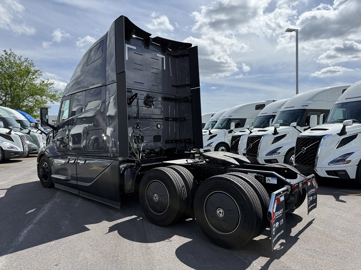 Rear driver side view of a gray 2025 Volvo VNL64T860 sleeper semi truck showing the aerodynamic cab extenders and tandem drive axles.