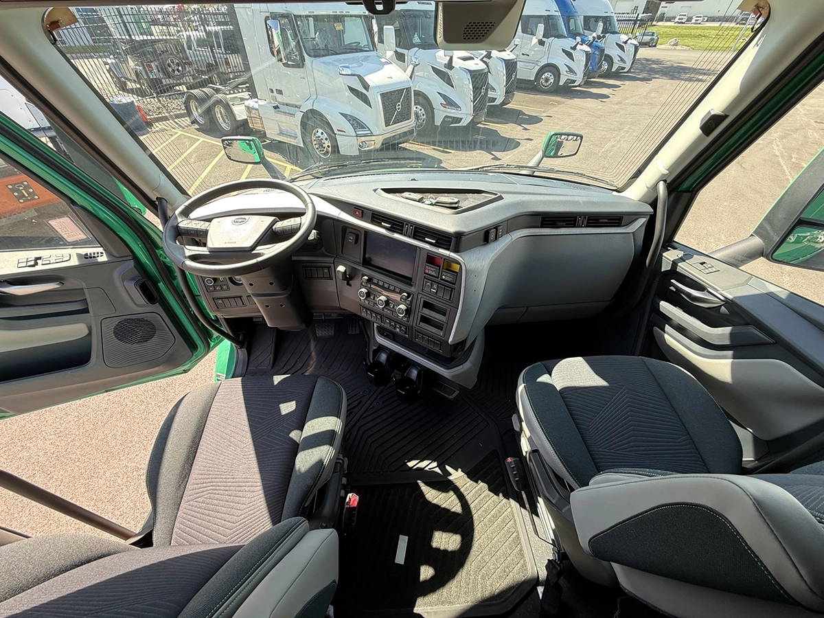 Interior cab view of a 2025 Volvo VNL64T860 showing the dashboard, touchscreen infotainment display, center controls, and two cloth seats.