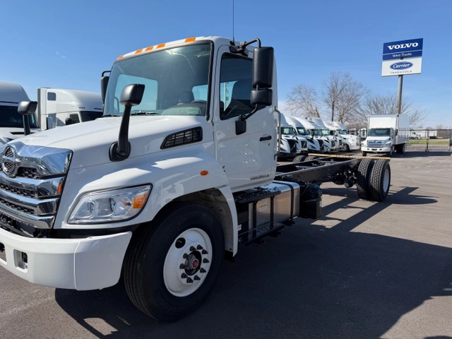 Front driver side view of a white 2026 Hino L6 conventional cab and chassis truck with a chrome grille and exposed frame rails, parked at Gateway Truck & Refrigeration.