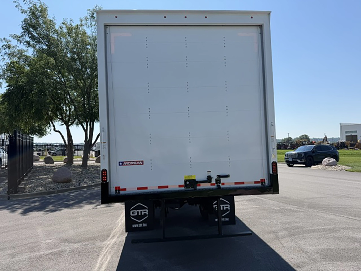 Rear view of a white 2026 Hino L6 box truck with a Morgan roll-up rear door, GTR mud flaps, and reflective tape along the bumper.