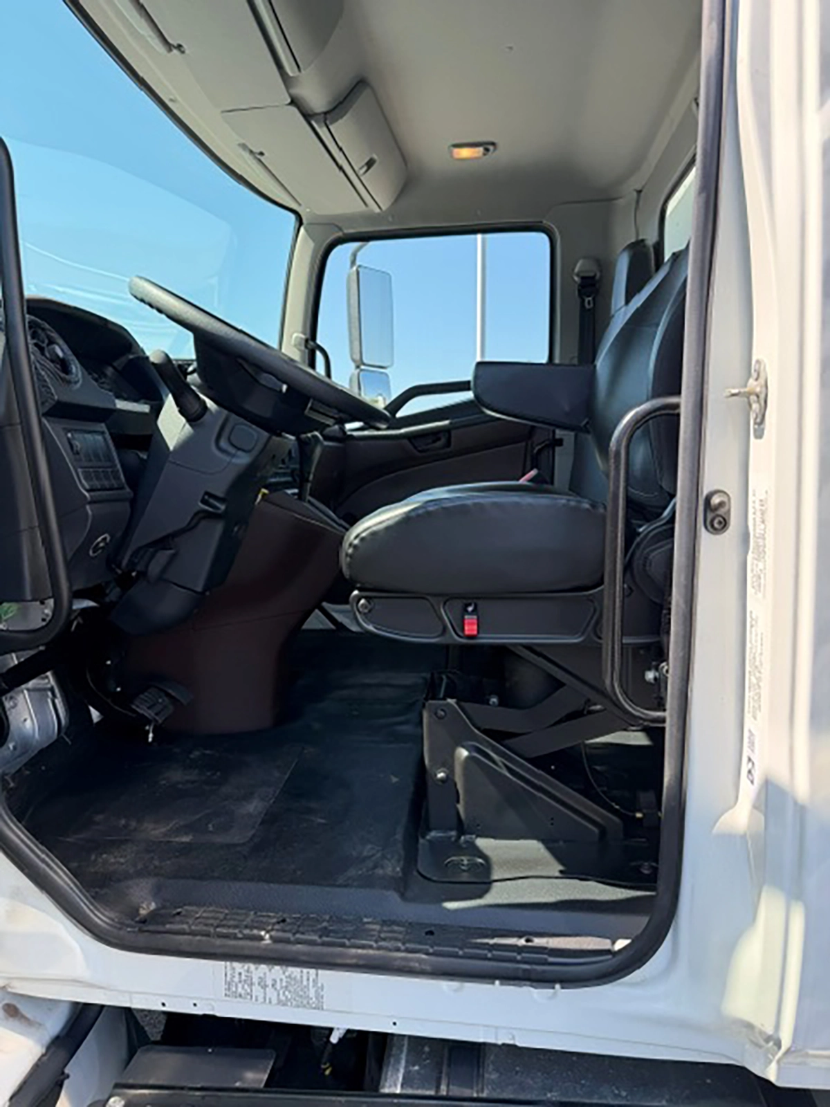 Interior cab view of a 2026 Hino L6 showing black seating, the steering wheel, and dashboard through the open driver door.