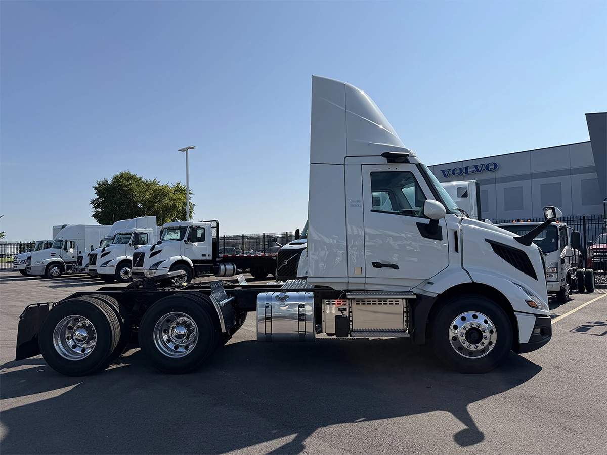 Driver-side profile view of a white Volvo day cab truck tractor with tandem rear axles, chrome wheels, and a raised roof fairing, parked at the Gateway Truck & Refrigeration Collinsville lot.