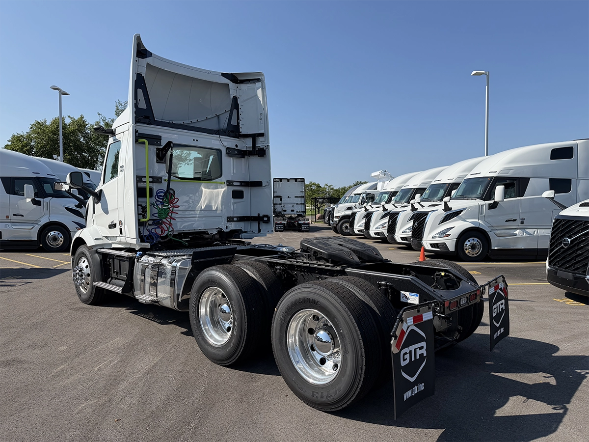 ear driver-side view of a white Volvo day cab truck tractor with the cab tilted forward, showing tandem axles, chrome wheels, and GTR-branded mud flaps, parked at Gateway Truck & Refrigeration.