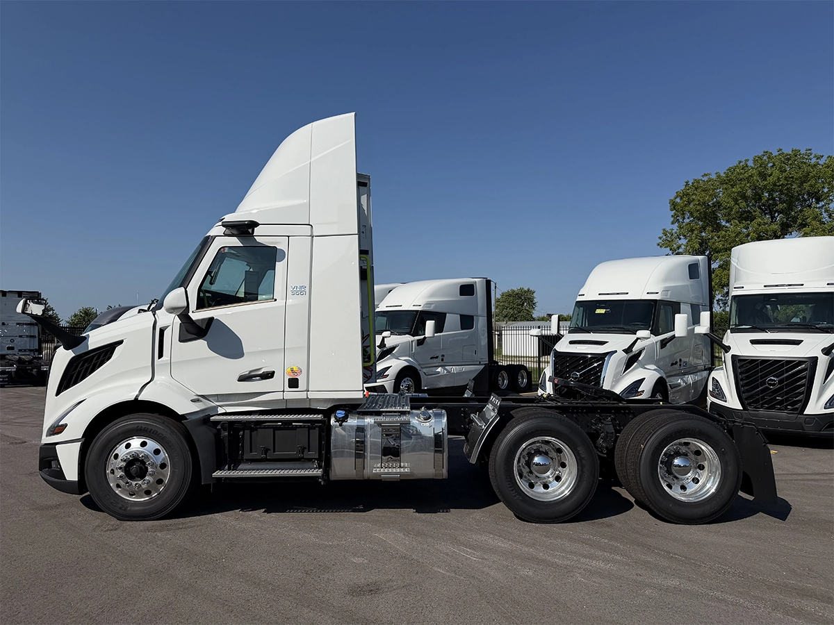Driver-side profile view of a white Volvo VNR day cab truck tractor with a raised roof fairing, tandem rear axles, and polished aluminum fuel tank, parked among other Volvo trucks at Gateway Truck & Refrigeration.